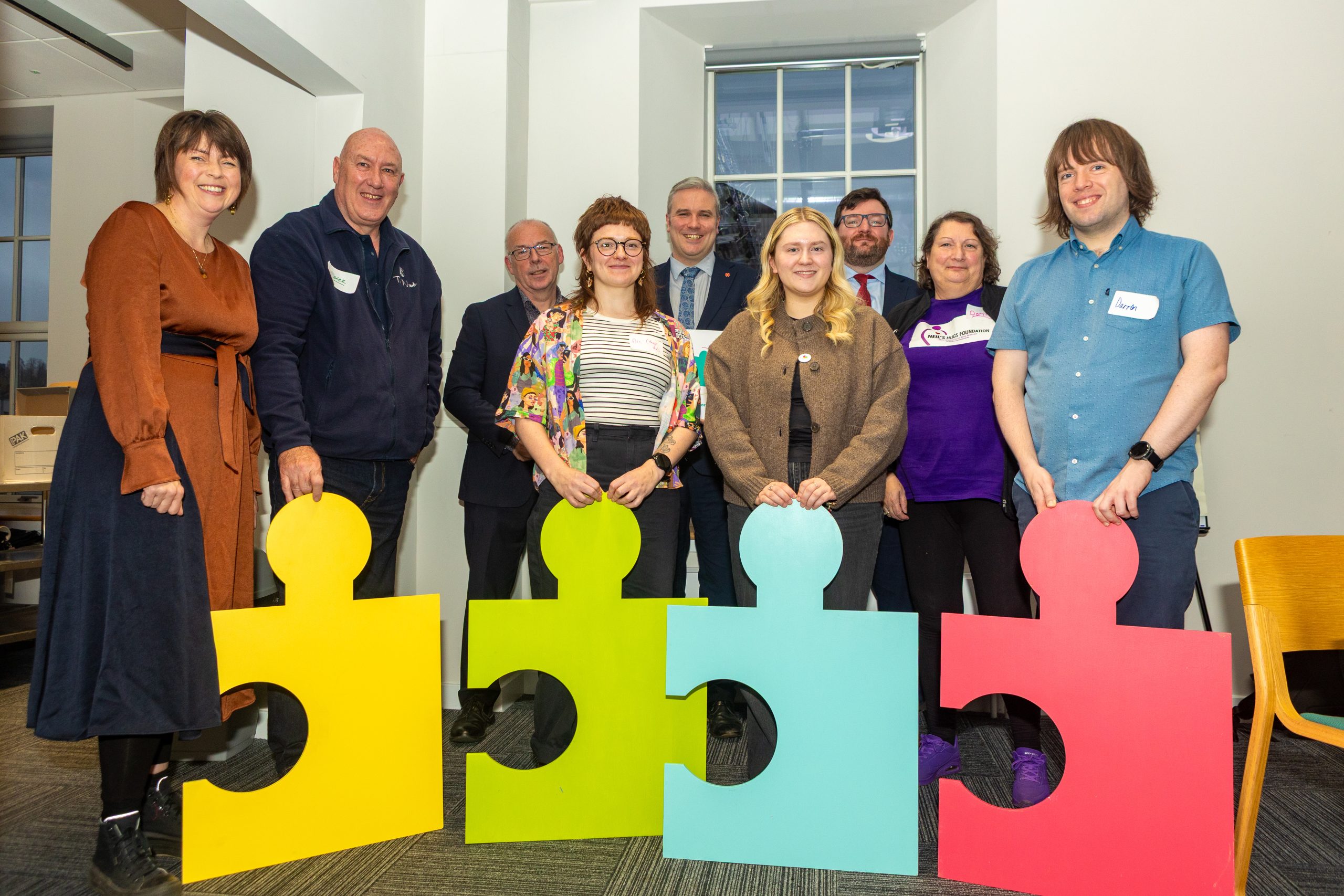 A group of people standing for a photo with four different coloured giant jigsaw pieces.